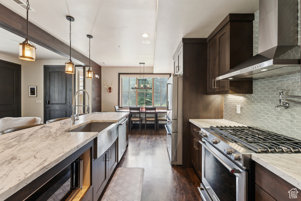 Kitchen with stainless steel appliances, wall chimney exhaust hood, a sink, dark brown cabinets, and light stone counters