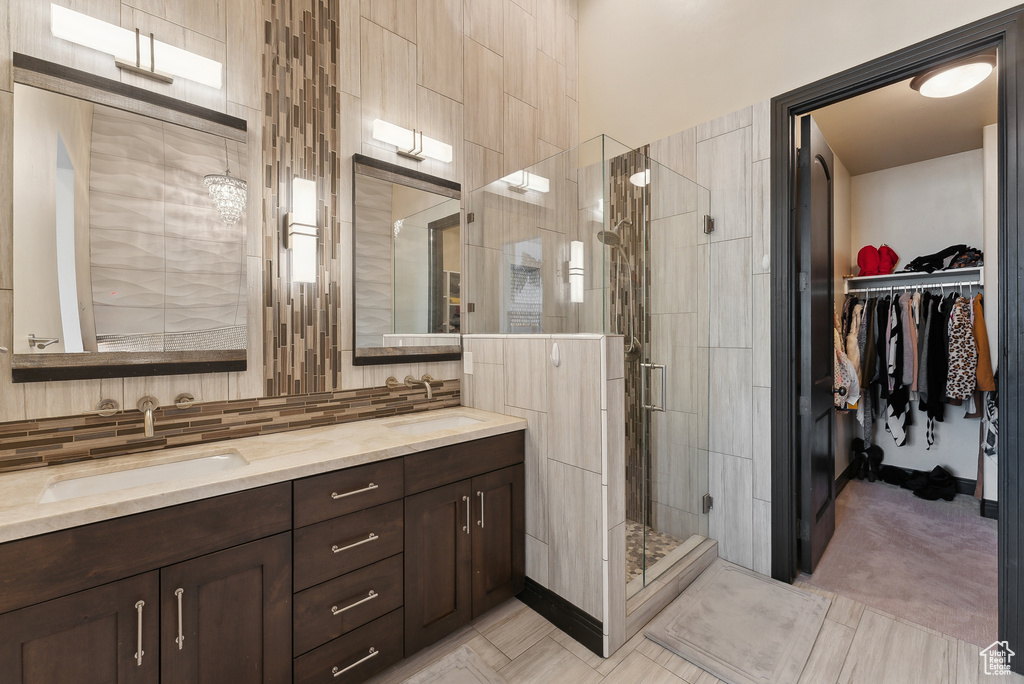 Full bathroom featuring a shower stall, double vanity, a walk in closet, and backsplash