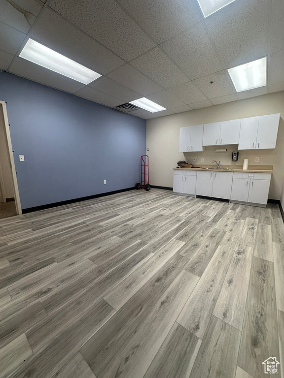 Unfurnished living room featuring a drop ceiling, light wood-style floors, baseboards, and a sink