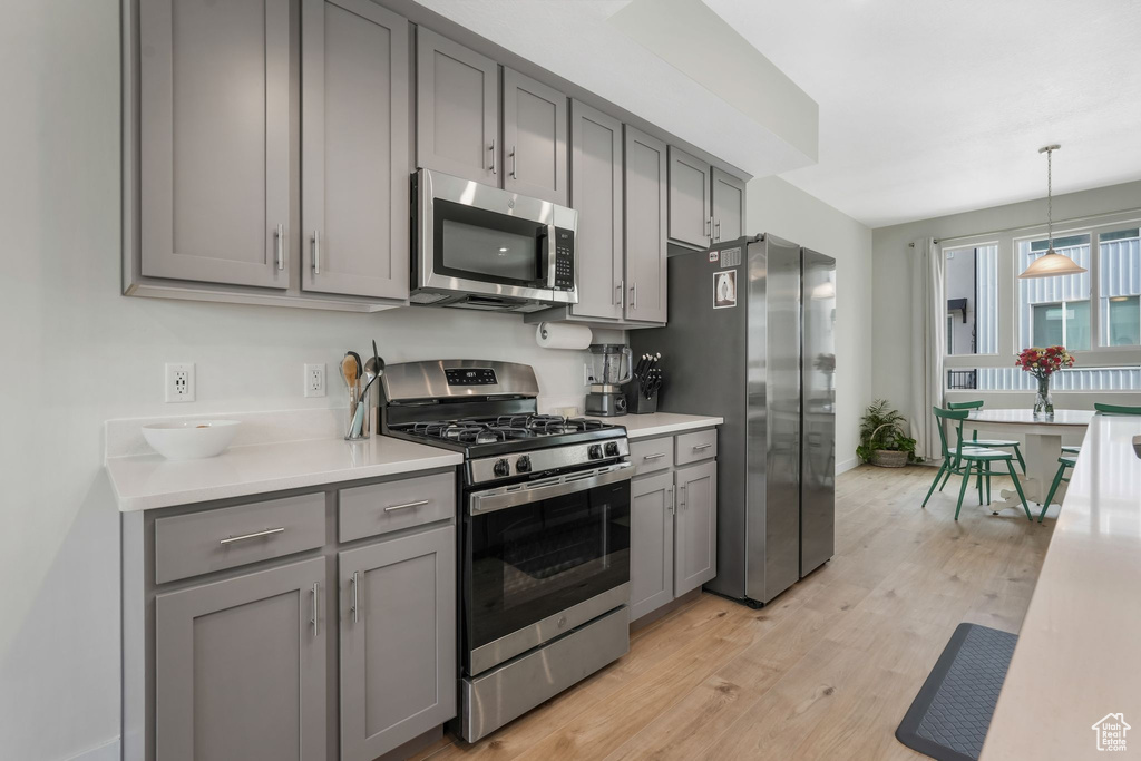Kitchen featuring appliances with stainless steel finishes, gray cabinetry, light countertops, light wood-style floors, and baseboards