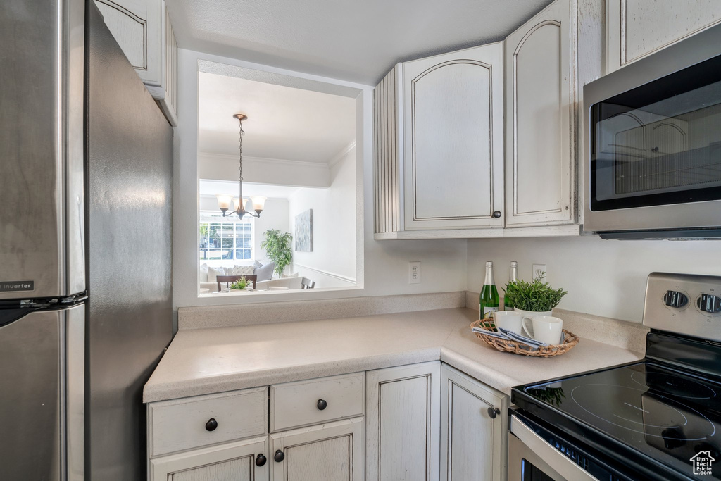 Kitchen featuring stainless steel appliances, white cabinetry, a chandelier, ornamental molding, and light countertops