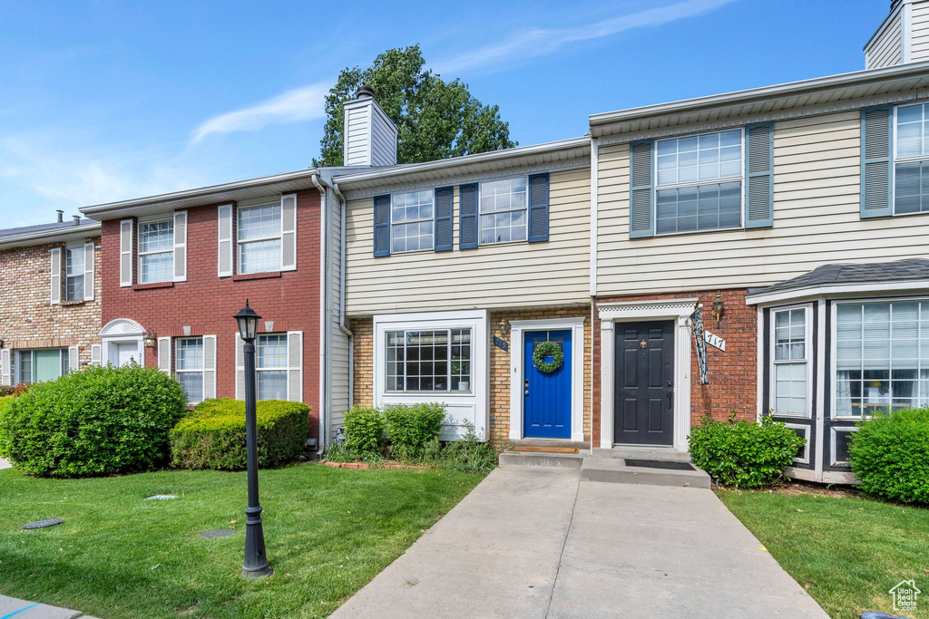 Townhome / multi-family property featuring a chimney, a front lawn, and brick siding