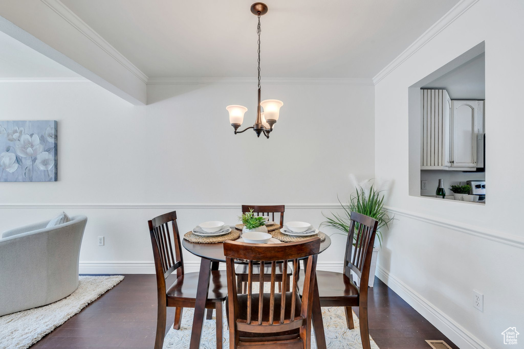 Dining space featuring a chandelier, crown molding, dark wood-style flooring, and baseboards