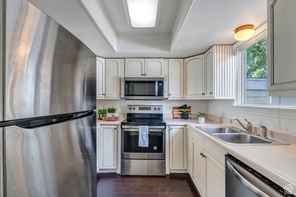 Kitchen featuring appliances with stainless steel finishes, a sink, light countertops, and a tray ceiling