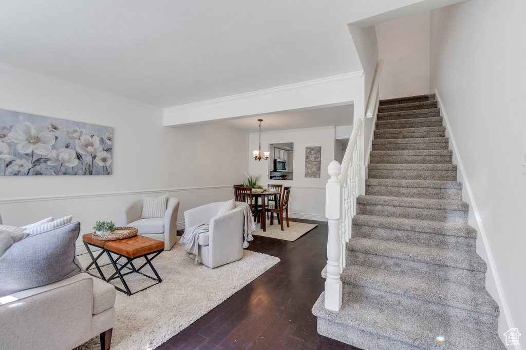 Living area with stairway, wood finished floors, ornamental molding, and a chandelier