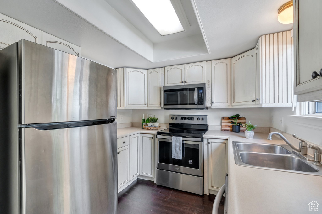 Kitchen featuring appliances with stainless steel finishes, a sink, light countertops, dark wood finished floors, and a raised ceiling