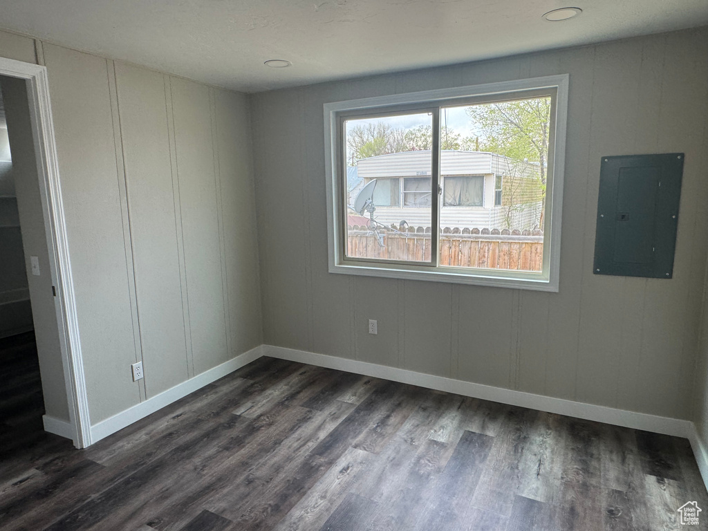Spare room featuring baseboards, electric panel, and dark wood-type flooring