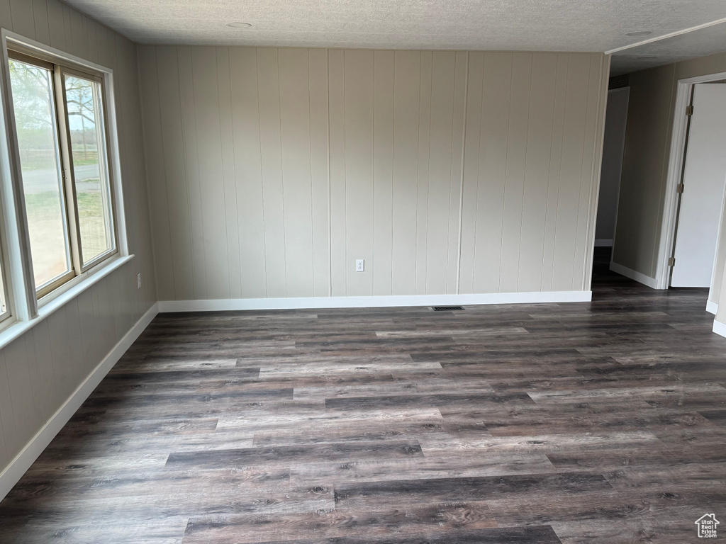 Unfurnished room featuring a textured ceiling, dark wood-style flooring, baseboards, and visible vents