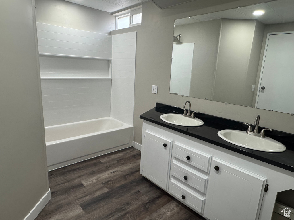 Bathroom with bathtub / shower combination, double vanity, a sink, and wood finished floors