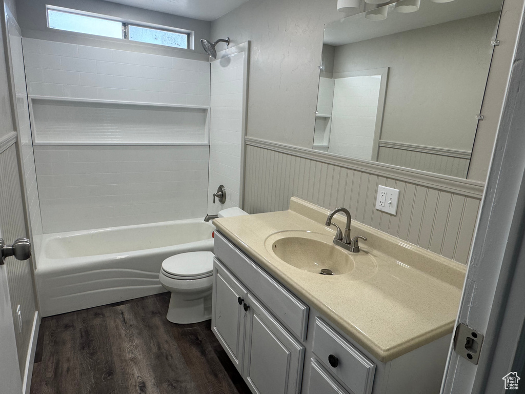 Full bath featuring shower / bath combination, toilet, wainscoting, vanity, and wood finished floors