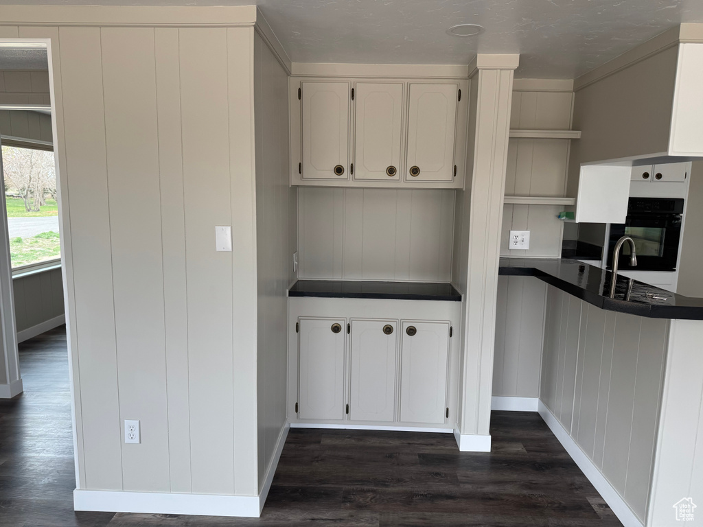 Kitchen with dark countertops, oven, white cabinetry, dark wood-type flooring, and baseboards