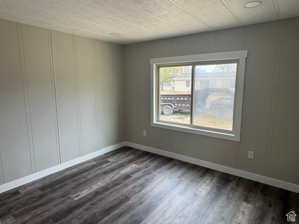 Unfurnished room featuring dark wood finished floors, a decorative wall, baseboards, and a textured ceiling
