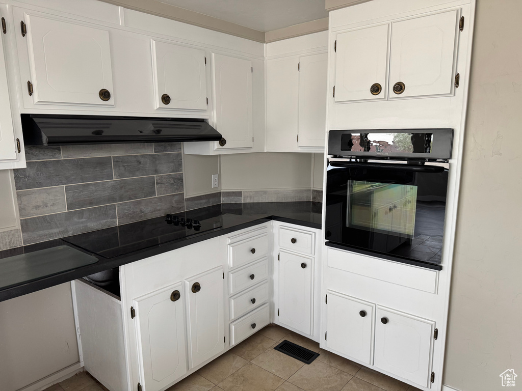 Kitchen featuring under cabinet range hood, white cabinetry, backsplash, dark countertops, and oven
