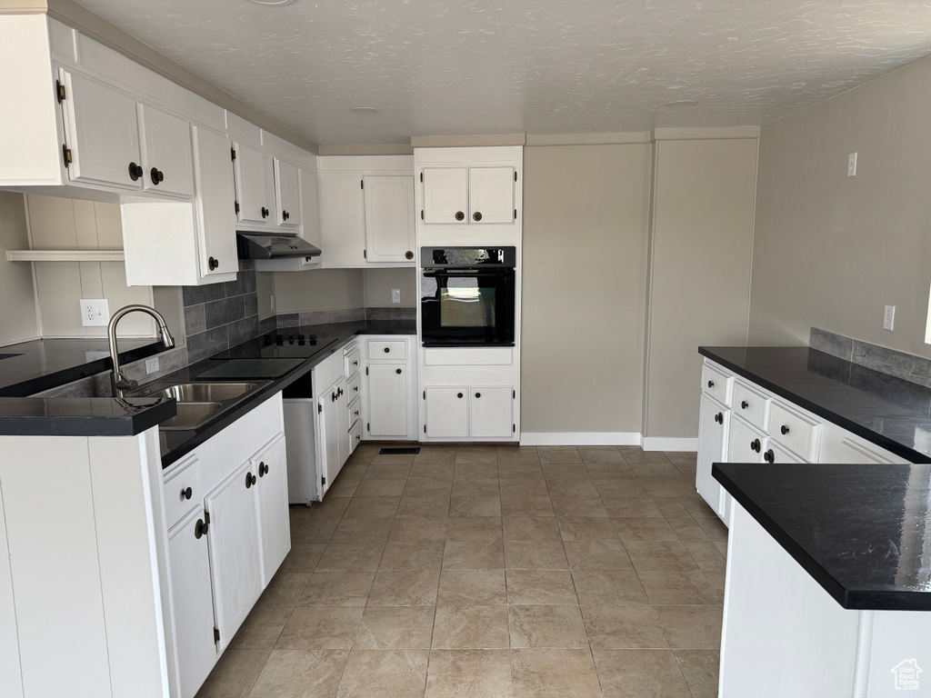 Kitchen with a textured ceiling, under cabinet range hood, white cabinetry, black appliances, and dark countertops