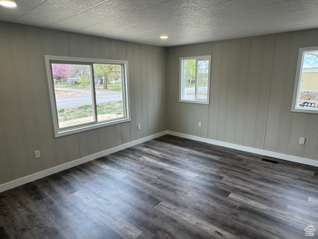 Empty room with dark wood-style floors and visible vents