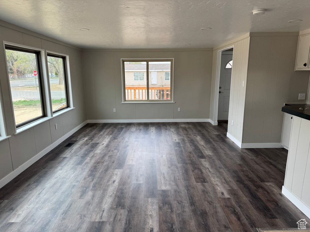 Unfurnished living room featuring dark wood-style flooring, a wealth of natural light, and a decorative wall