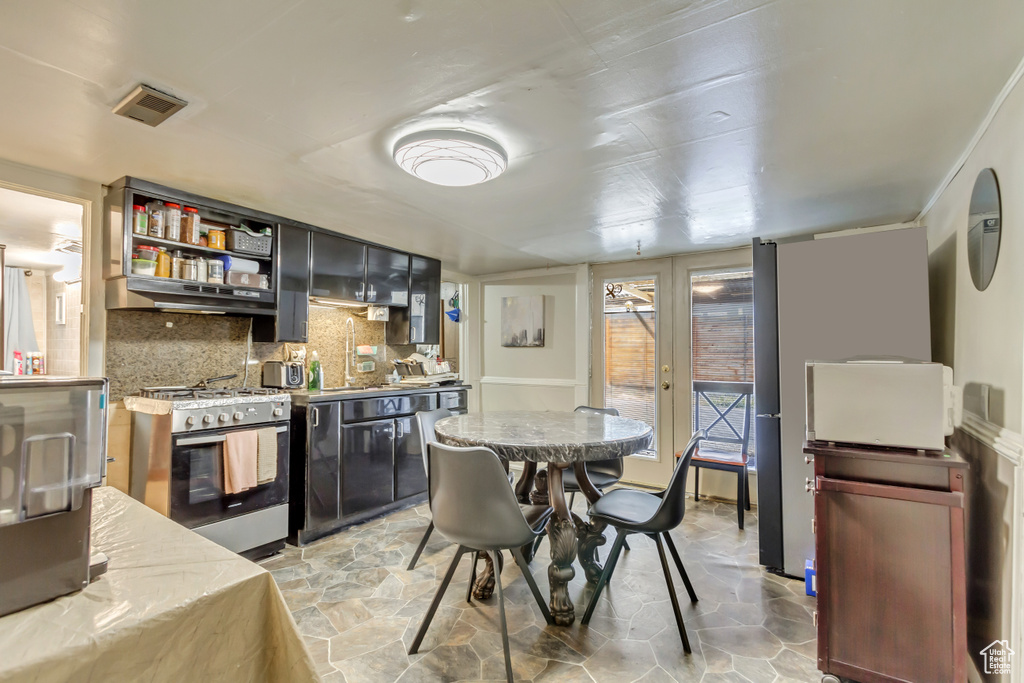 Kitchen with stainless steel gas stove, under cabinet range hood, light stone finish flooring, tasteful backsplash, and light countertops