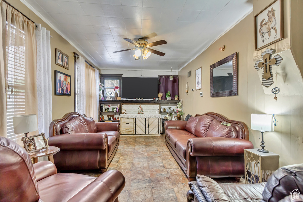 Living room with ornamental molding, a ceiling fan, and light stone finish flooring