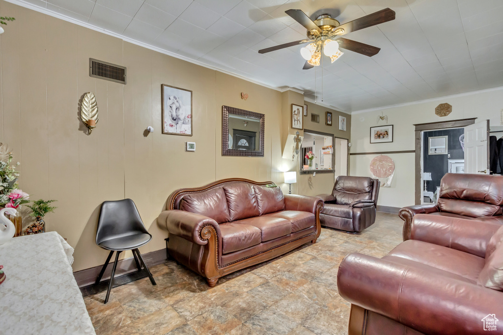 Living room featuring ceiling fan, stone finish floors, ornamental molding, and baseboards