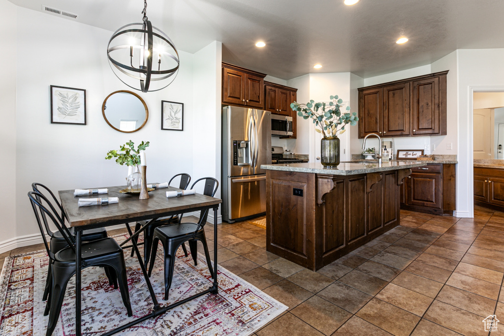 Kitchen with stainless steel appliances, a sink, an island with sink, a breakfast bar area, and light stone countertops