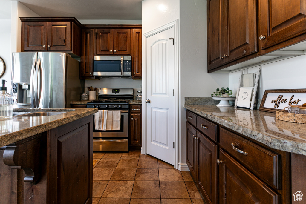 Kitchen with stainless steel appliances, dark brown cabinets, stone countertops, and dark tile patterned floors
