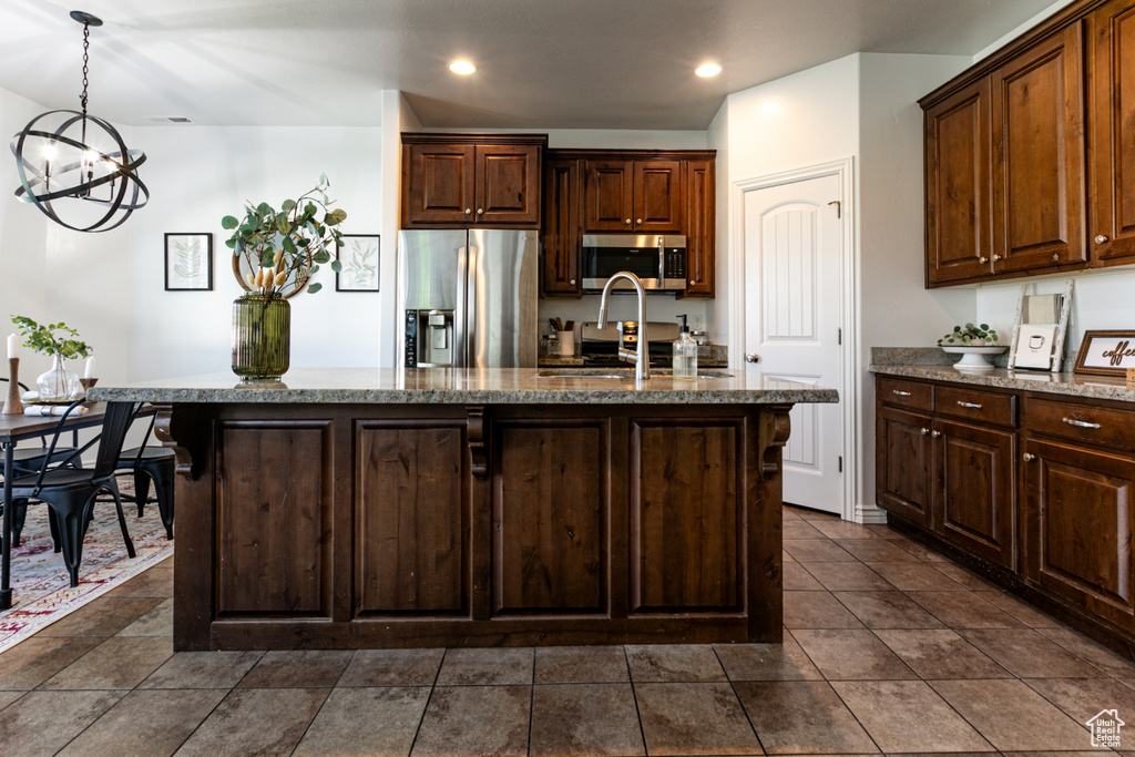 Kitchen with appliances with stainless steel finishes, a chandelier, stone countertops, a center island with sink, and a sink