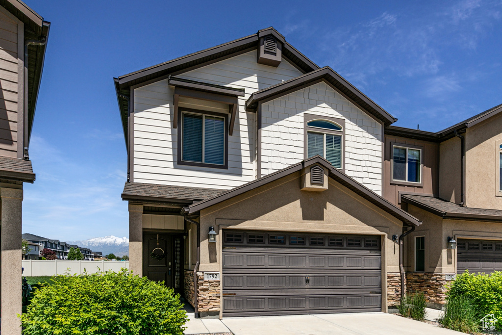 View of front of home featuring stone siding, driveway, a garage, and fence
