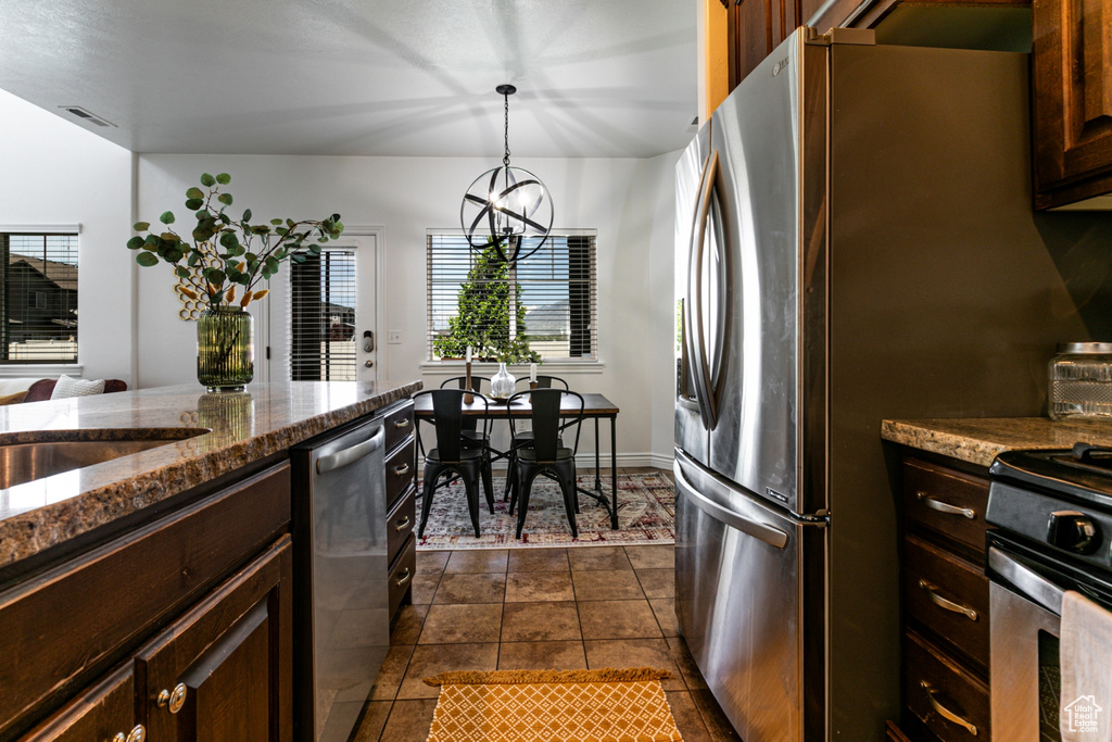 Kitchen with appliances with stainless steel finishes, healthy amount of natural light, dark tile patterned flooring, and dark stone countertops