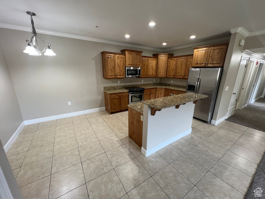 Kitchen with stainless steel appliances, brown cabinets, a kitchen bar, dark stone countertops, and ornamental molding