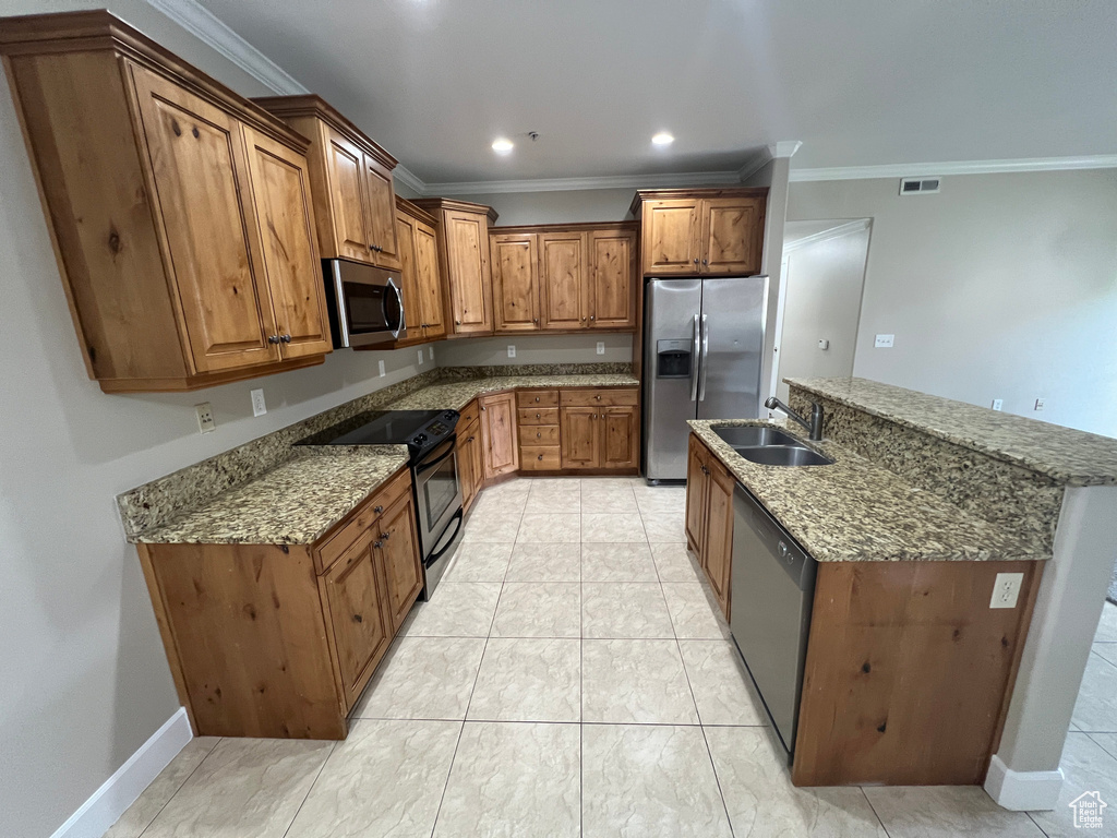 Kitchen with appliances with stainless steel finishes, a sink, brown cabinetry, crown molding, and an island with sink