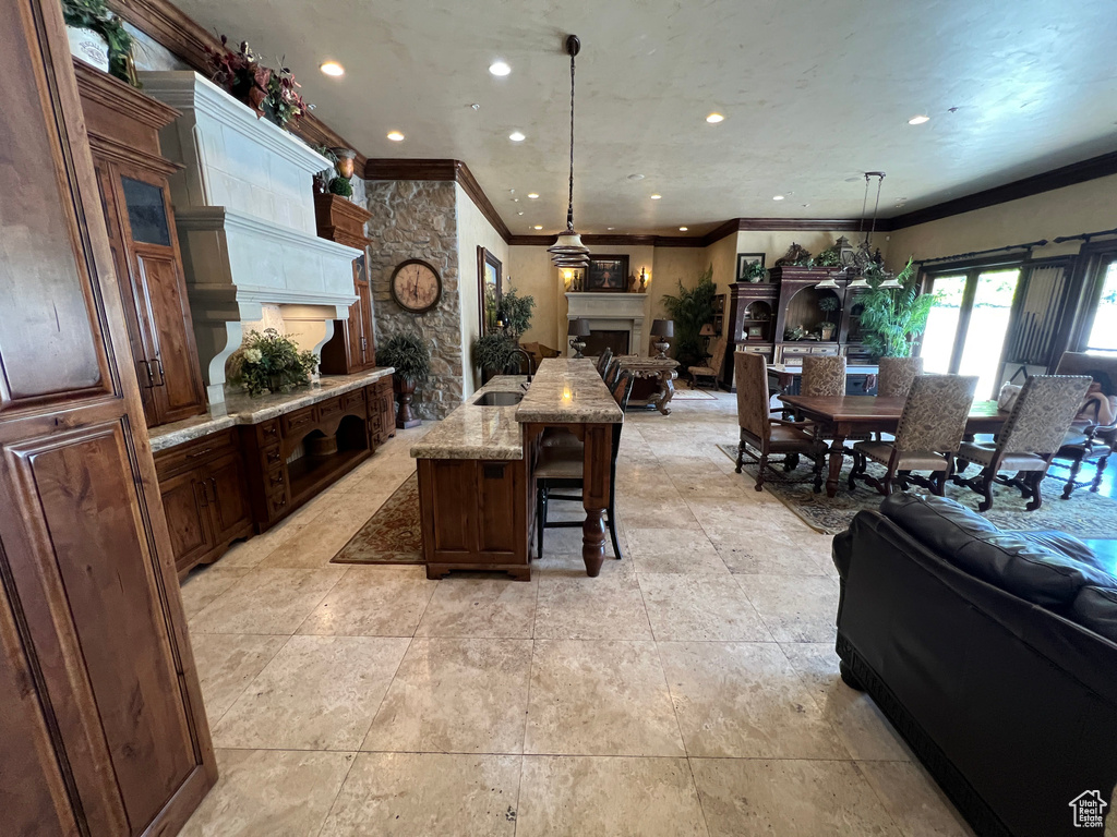 Kitchen with open floor plan, a fireplace, crown molding, a breakfast bar, and light stone countertops