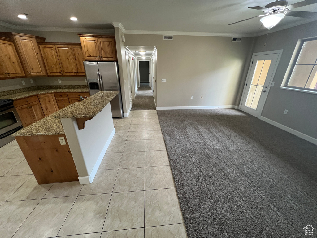 Kitchen with stainless steel fridge with ice dispenser, brown cabinets, range, crown molding, and dark stone counters