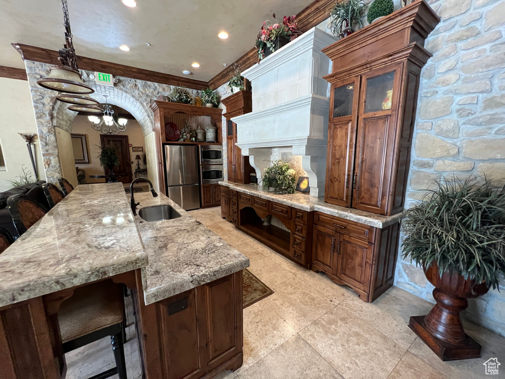 Kitchen featuring appliances with stainless steel finishes, a sink, a chandelier, a breakfast bar area, and light stone countertops