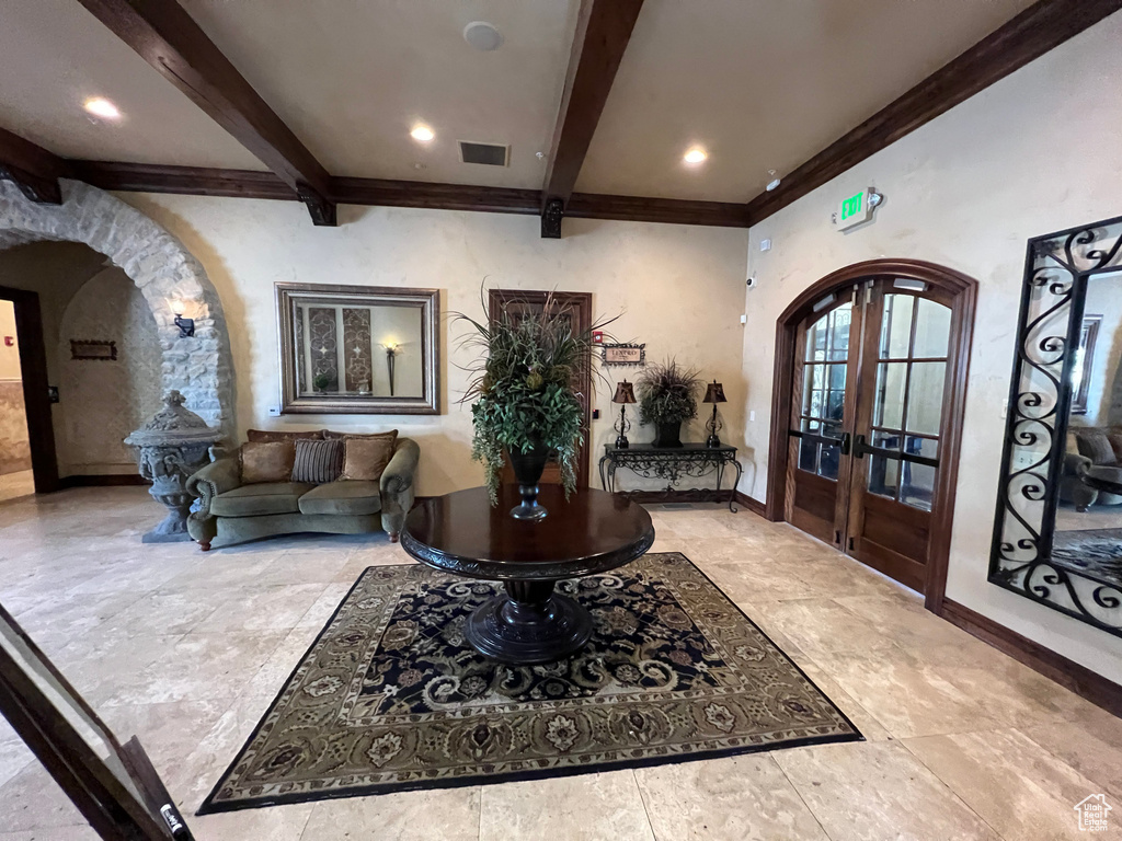 Entrance foyer featuring arched walkways, beam ceiling, french doors, baseboards, and crown molding