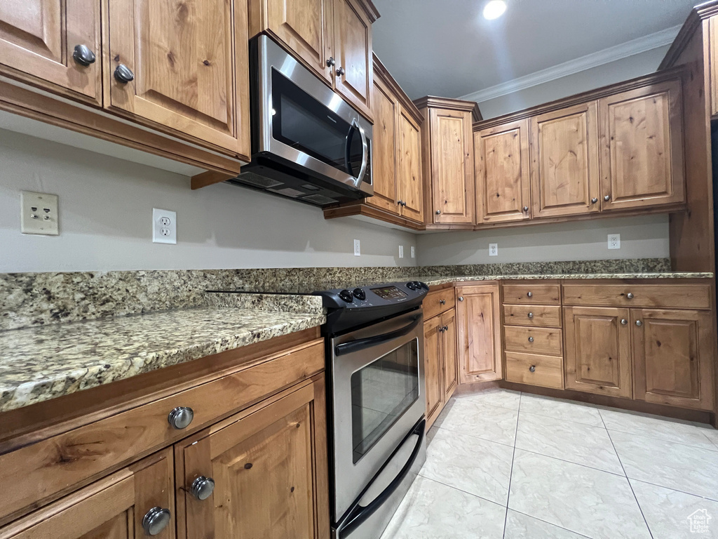 Kitchen with appliances with stainless steel finishes, ornamental molding, dark stone counters, and brown cabinetry