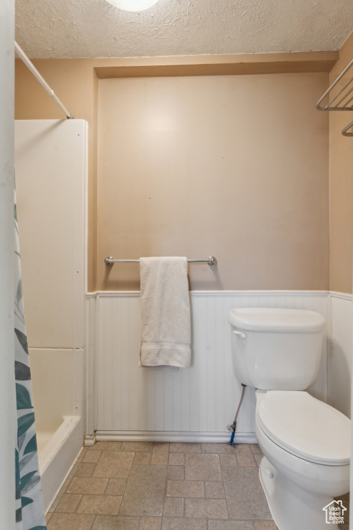 Bathroom featuring a textured ceiling, a wainscoted wall, toilet, stone finish floors, and shower / bath combo