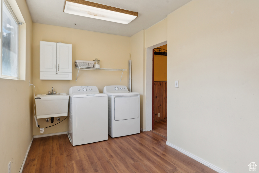 Clothes washing area featuring washing machine and dryer, wood finished floors, cabinet space, and baseboards