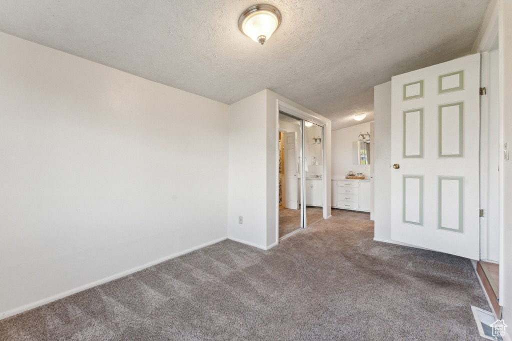 Unfurnished bedroom featuring carpet floors, a textured ceiling, baseboards, and connected bathroom