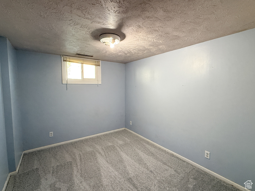 Basement featuring a textured ceiling, carpet, and baseboards