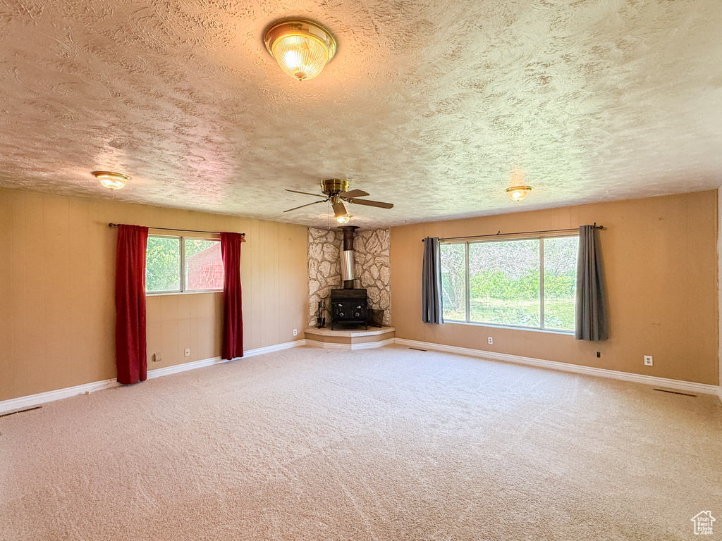 Unfurnished living room featuring a wood stove, a textured ceiling, baseboards, and carpet
