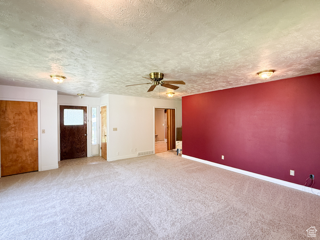 Carpeted spare room with a textured ceiling, ceiling fan, and baseboards