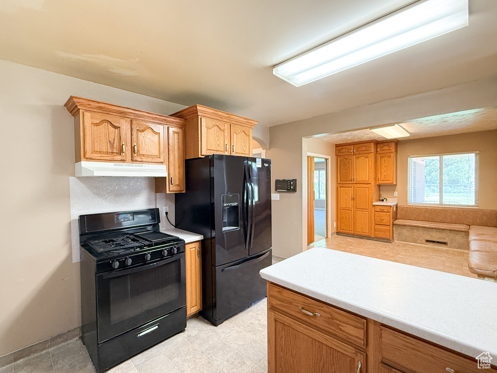 Kitchen with black appliances, under cabinet range hood, light countertops, and baseboards