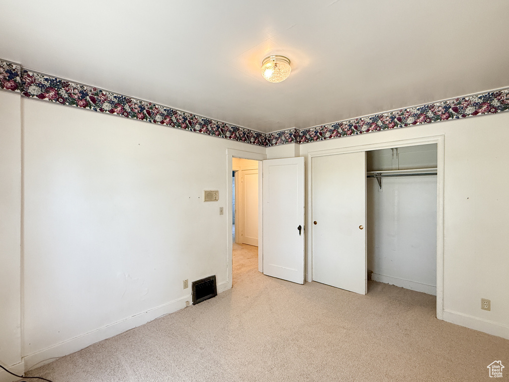 Unfurnished bedroom featuring light colored carpet, baseboards, and a closet