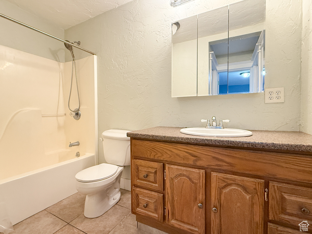 Bathroom featuring a textured wall, tile patterned floors, toilet, vanity, and shower / bath combination