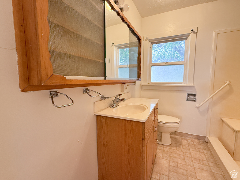 Bathroom with toilet, vanity, stone finish flooring, and baseboards
