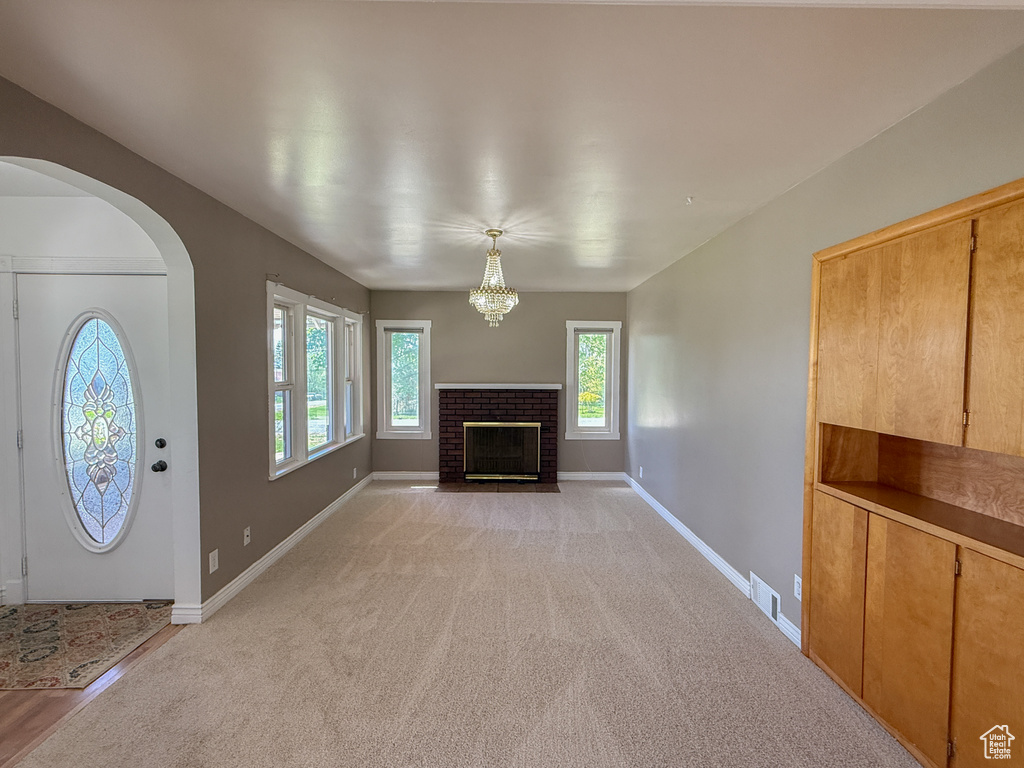 Unfurnished living room featuring a fireplace, light carpet, arched walkways, baseboards, and a chandelier
