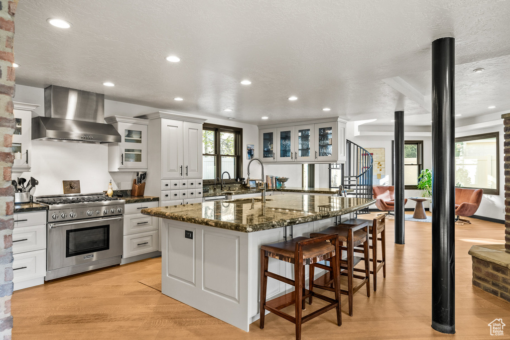 Kitchen featuring high end range, wall chimney exhaust hood, a breakfast bar area, a sink, and recessed lighting