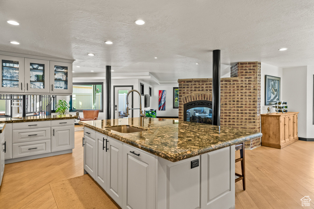Kitchen with a sink, light wood finished floors, recessed lighting, an island with sink, and a textured ceiling