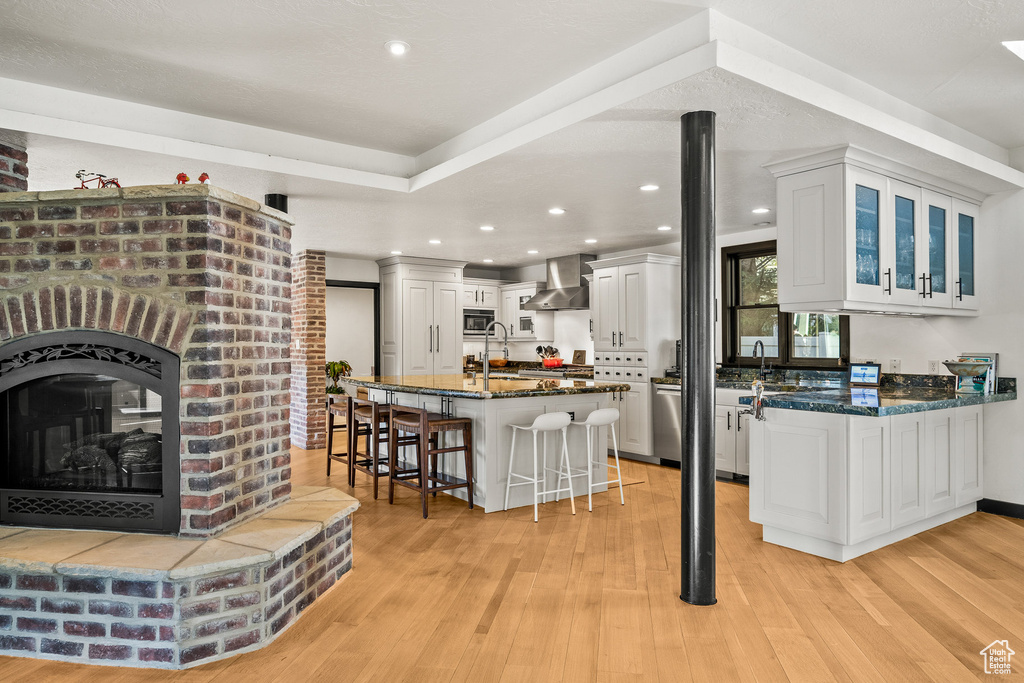 Kitchen featuring wall chimney exhaust hood, stainless steel appliances, a kitchen bar, a sink, and dark stone countertops