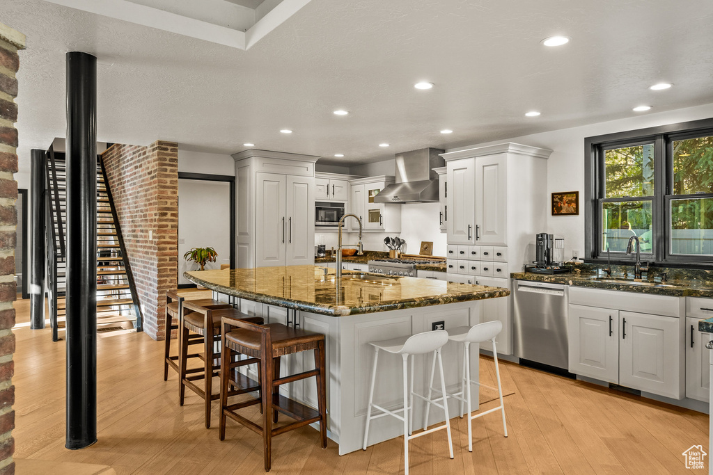 Kitchen featuring stainless steel appliances, a sink, wall chimney range hood, a breakfast bar area, and recessed lighting